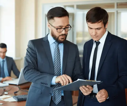 Two male business consultants in suits reviewing a clipboard in an office setting